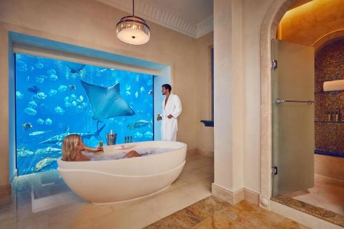 Atlantis, The Palm في دبي: رجل في حوض استحمام في حمام مع حوض للأسماك
