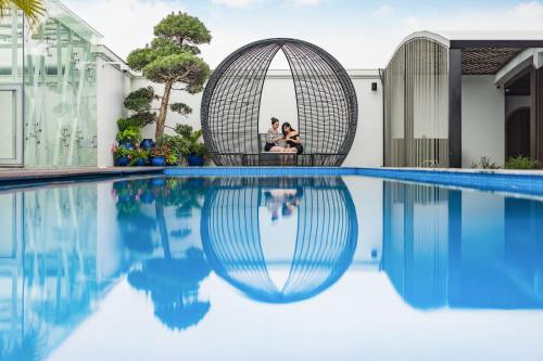 a couple sitting in a wicker chair next to a swimming pool at Grand Fleuve Boutique in Ha Long