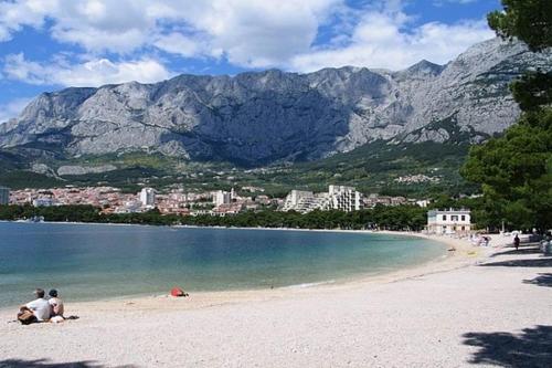 a group of people sitting on a beach with mountains at Apartmani Sea Star in Makarska