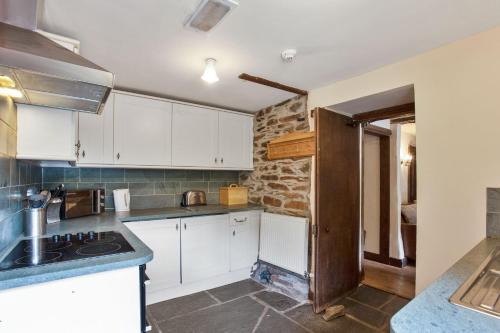 a kitchen with white cabinets and a stone wall at The Mountain Cottages - Pelton Wheel in Coniston