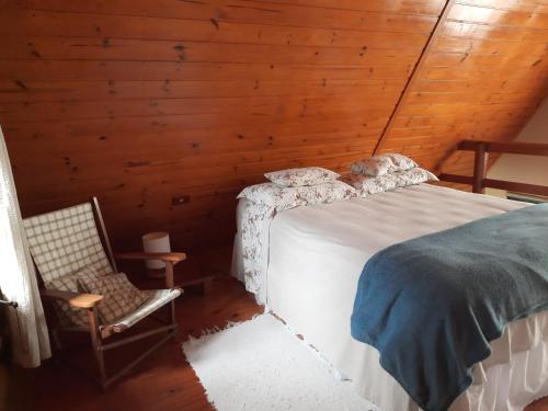 ein Schlafzimmer mit einem Bett und einem Stuhl in einer Hütte in der Unterkunft Nosso Pátio - Chalé na Montanha in Rancho Queimado