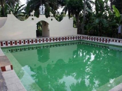 a swimming pool with green water in front of a building at Indeco Hotels Swamimalai in Kumbakonam