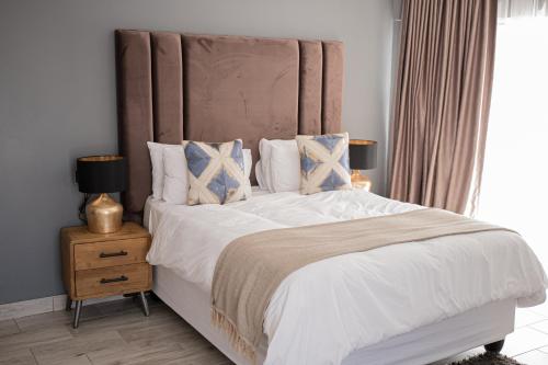 Gletwyn Boutique Guesthouse في هراري: غرفة نوم بسرير كبير مع شراشف بيضاء ومخدات زرقاء