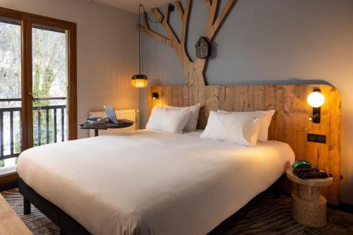 a bedroom with a large white bed with a tree on the wall at ibis Styles Les Houches Chamonix in Les Houches