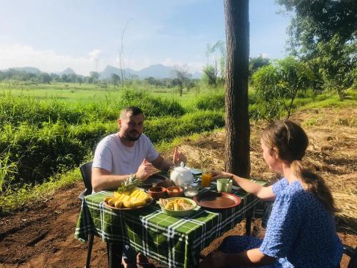 Ein Mann und ein Mädchen sitzen an einem Picknicktisch mit Essen in der Unterkunft The wild culture in Sigiriya