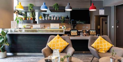 un restaurante con 2 sillas y un bar con almohadas amarillas en Heeton Concept Hotel - Kensington London, en Londres