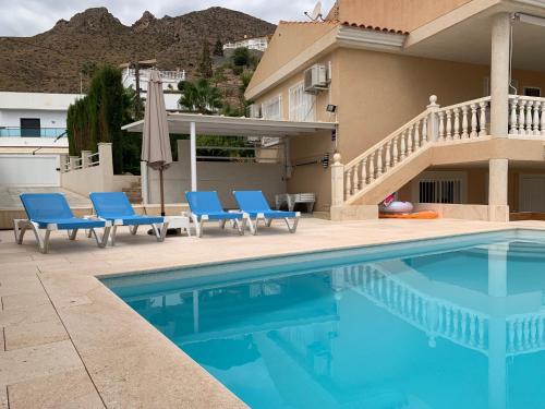 a swimming pool with blue chairs and a house at Agradable casa con piscina in Bolnuevo