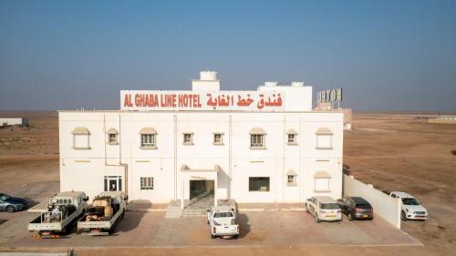 Un gran edificio blanco con coches aparcados en un estacionamiento. en Al Ghaba Line Hotel, en Al Ghābah