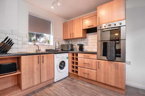 cocina con armarios de madera, lavadora y secadora en Victoria Gardens, en Colchester