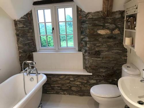 a bathroom with a tub and a toilet and a window at Hallgarden Farmhouse in Otterham