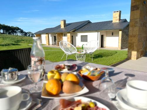 une table avec des assiettes de nourriture et une maison dans l'établissement El Pueblín del Pinar, à Navia