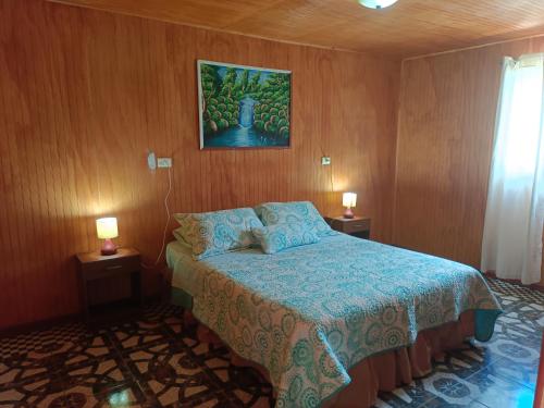 a bedroom with a bed with a blue bedspread and two lamps at cabañas Te Pito Kura in Hanga Roa