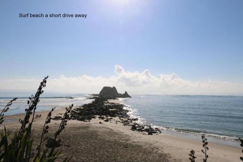 a view of the beach with a rock in the ocean at Cosy Mangawhai House in Mangawhai