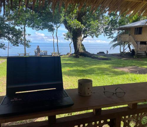 laptopa siedzącego na stole z kubkiem i kieliszkami w obiekcie Borbon's Treehouse By the Sea w Mambajao
