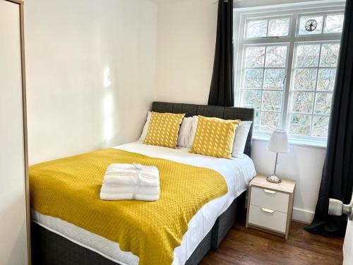 sypialnia z łóżkiem z żółtym kocem i oknem w obiekcie LONDON KENNINGTON / OVAL APARTMENTS w Londynie