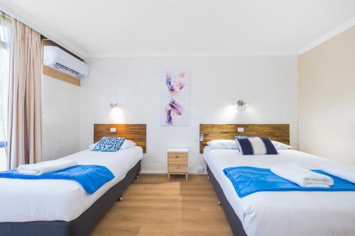 two beds in a room with white walls and wooden floors at Plainsman Motel in Forbes