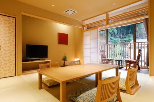 a dining room with a wooden table and a balcony at Yuraku Kinosaki Spa & Gardens in Toyooka