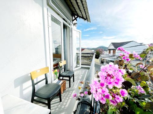 a balcony with pink flowers and chairs on a house at Môn Bạc Home in Da Lat