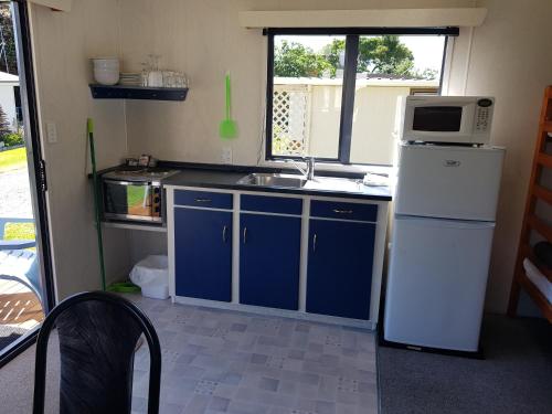 a kitchen with blue cabinets and a white refrigerator at Te Puru Holiday Park in Thames