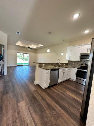 an empty kitchen with white cabinets and wood floors at getAway Home in Lehigh Acres