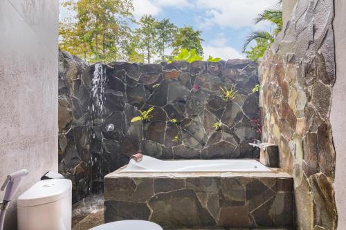 Thalassa Dive & Wellbeing Resort Manado في مانادو: حمام بحائط حجري وحوض استحمام