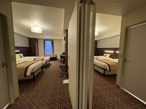 a hotel room with three beds and a hallway at Hotel Monterey Fukuoka in Fukuoka