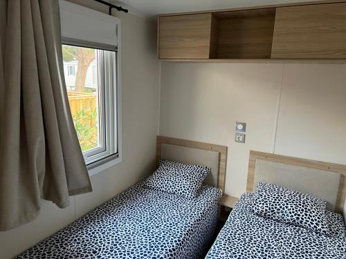 twee bedden in een kamer met een raam bij Mobil Home Bleu ‘n’ Blue in Canet-en-Roussillon