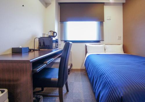 a bedroom with a desk with a bed and a microwave at HOTEL LiVEMAX Kanazawa Ekimae in Kanazawa