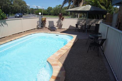 a swimming pool with a table and chairs and an umbrella at Beachside Motor Inn in Hervey Bay