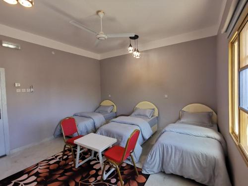 a room with four beds and a table and chairs at Al Hamra Guest House in Al Ḩamrāʼ