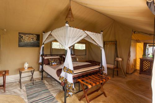 1 dormitorio con cama con dosel en una tienda de campaña en Gnu Ndutu Camp, en Sinoni