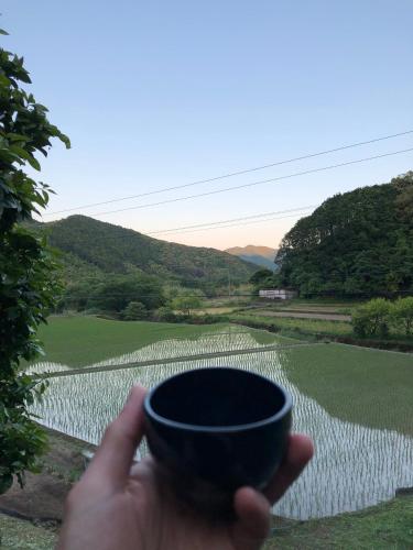 a person holding a cup in front of a field at Shimanto Riverside Hideaway in Shimanto