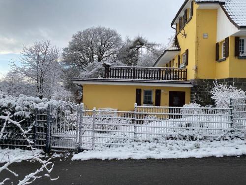a yellow house with a fence in the snow at Wollmeiner's Lodge in Arnsberg
