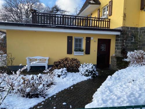 a yellow house with a white bench in the snow at Wollmeiner's Lodge in Arnsberg