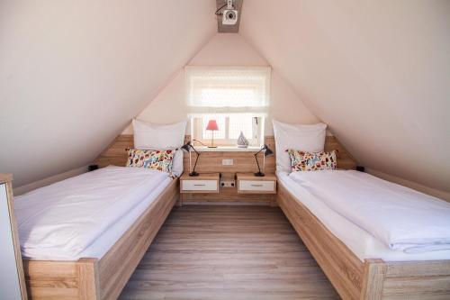 2 Betten in einem Dachzimmer mit Fenster in der Unterkunft Up Besöök - Sanddorn mit Infrarotsauna in Krummhörn