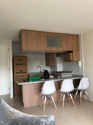 una cocina con 2 sillas blancas y una barra en condominio parquemar el tabo en El Tabo