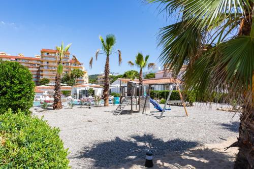 einen Spielplatz mit Schaukeln und Palmen am Strand in der Unterkunft Malgrat de Mar Beachfront Village in Malgrat de Mar