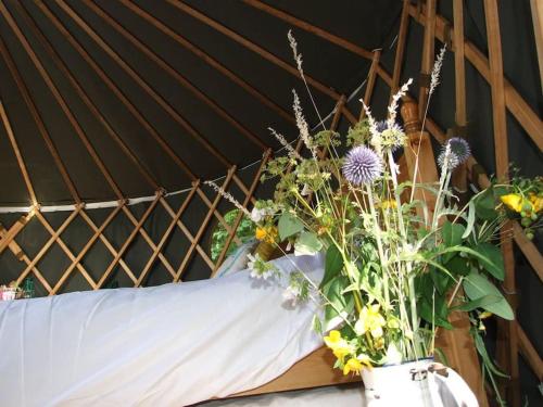 'Oak' Yurt in West Sussex countryside في Fernhurst: مزهرية مليئة بالورود فوق السرير