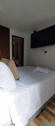 a bedroom with a large white bed with a tv on the wall at Hermoso apartamento en conjunto cerrado cerca al aeropuerto in Bogotá