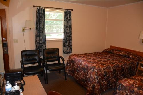 a hotel room with a bed and chairs and a window at The Village Motel in Richfield Springs