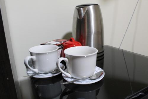 deux tasses à café et cuillères assises sur une étagère dans l'établissement Casa Leon 5 min away from the Airport, à Lima