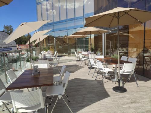 a patio with tables and white chairs and umbrellas at Hotel GRALTA in Jalostotitlán
