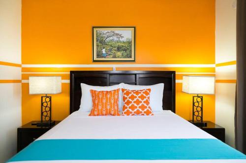 a bedroom with a bed with orange walls and two lamps at Hellshire Portmore Vacation Home in Portmore