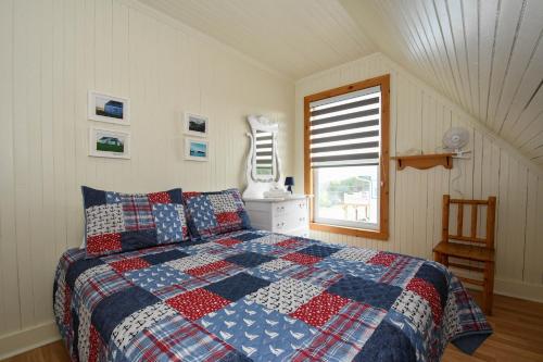 een slaapkamer met een quilt op een bed met een raam bij Maison de Percé in Perce