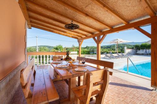 a wooden table and chairs on a patio with a pool at Vacation villa Matic with 7 bedrooms in Sinj