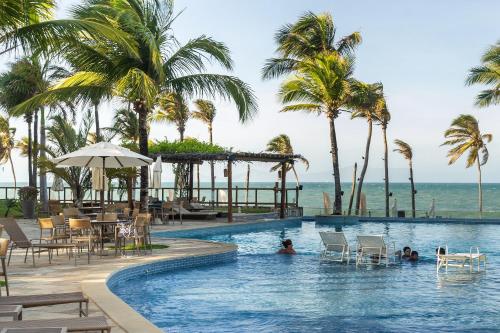 una piscina con palmeras y el océano en Apartamento Lindo e Completo - Wai Wai Cumbuco, en Cumbuco