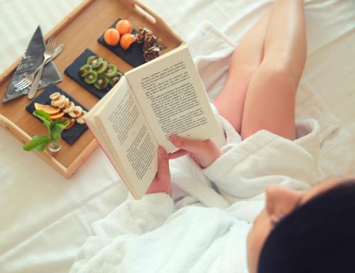a person laying on a bed reading a book at Kraal Hotel Vlore in Vlorë