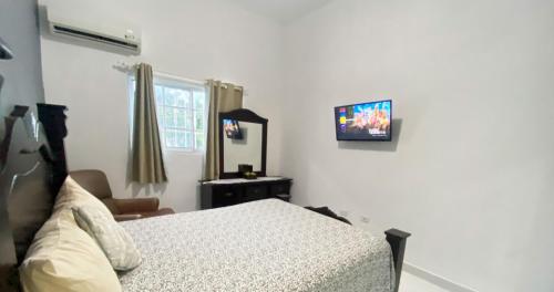 1 dormitorio con 1 cama y TV en la pared en Quiet Apartment, 3 Minutes From The Beach, 24H Security, Excellent Internet en San Felipe de Puerto Plata