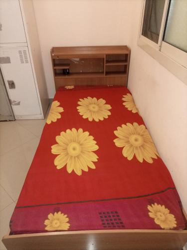 - un lit avec une couverture rouge et des fleurs jaunes dans l'établissement Mixed dormitory, only for Indians, à Charjah