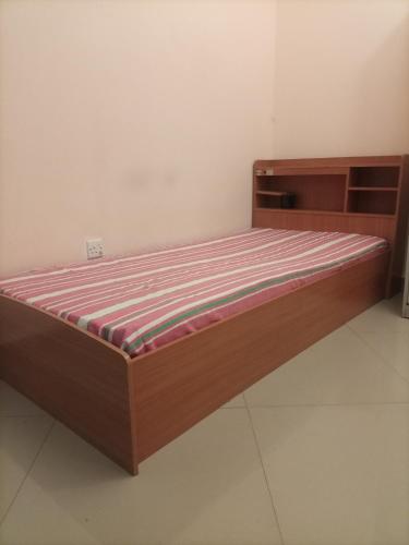 Cette chambre comprend un lit avec un cadre en bois. dans l'établissement Mixed dormitory, only for Indians, à Charjah